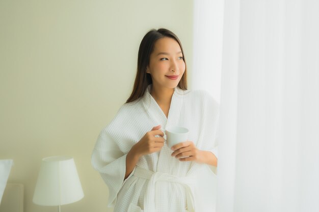 Portret mooie jonge Aziatische vrouwen met koffiekop in slaapkamer