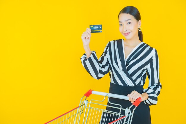 Portret mooie jonge aziatische vrouwenglimlach met kruidenierswinkelmand van supermarkt op geel