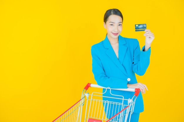 Portret mooie jonge aziatische vrouwenglimlach met kruidenierswinkelmand van supermarkt op geel