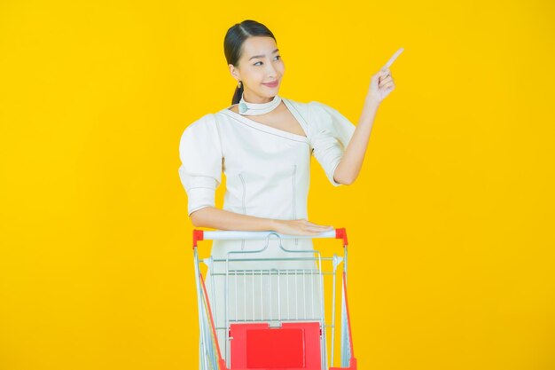 Portret mooie jonge aziatische vrouwenglimlach met kruidenierswinkelmand van supermarkt op kleurenachtergrond