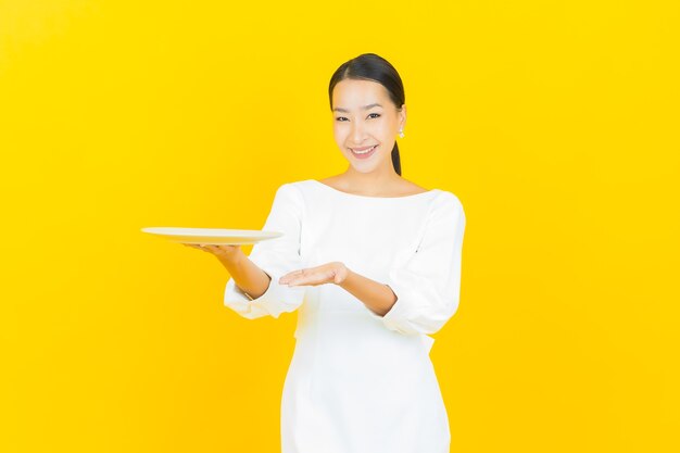 Portret mooie jonge aziatische vrouwenglimlach met lege plaatschotel op geel