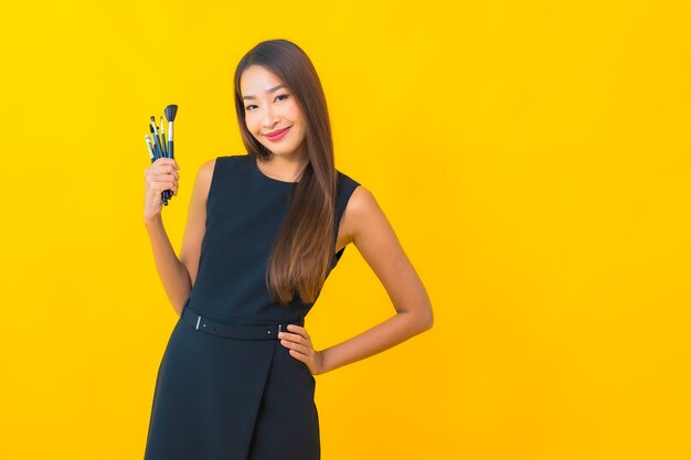 Portret mooie jonge Aziatische zakenvrouw met make-up cosmetische borstel op gele achtergrond