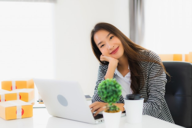 Portret mooie jonge Aziatische zakenvrouw werken vanuit huis met laptop mobiele telefoon met kartonnen doos klaar voor verzending