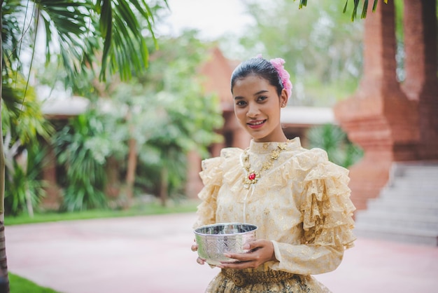 Gratis foto portret mooie vrouw in songkran-festival met thais traditioneel kostuum in de tempel met waterkom en glimlach thailand-cultuur met waterfestival