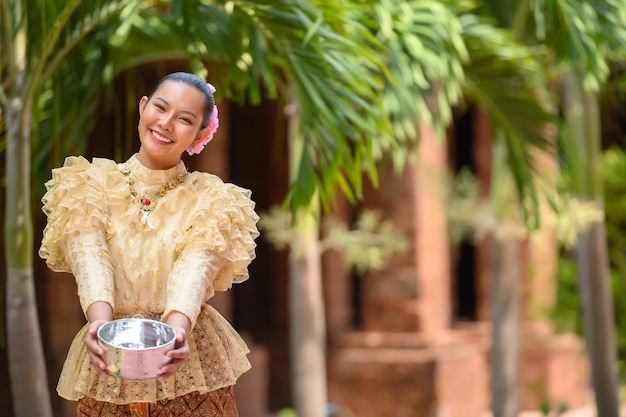 Gratis foto portret mooie vrouw in songkran-festival met thais traditioneel kostuum in de tempel met waterkom en glimlach thailand-cultuur met waterfestival