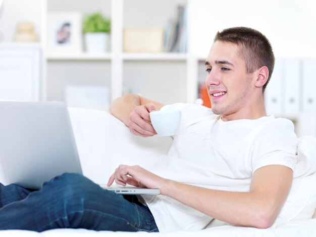 Portret profiel van lachende jonge man met kopje koffie met laptop thuis