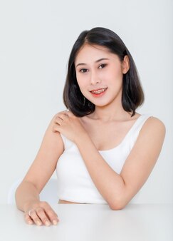 Portret schoonheid schot, close-up van millennial aziatische kort zwart haar model met make-up rode lip in tank top hemd zittend aan tafel poseren camera kijken op witte achtergrond.