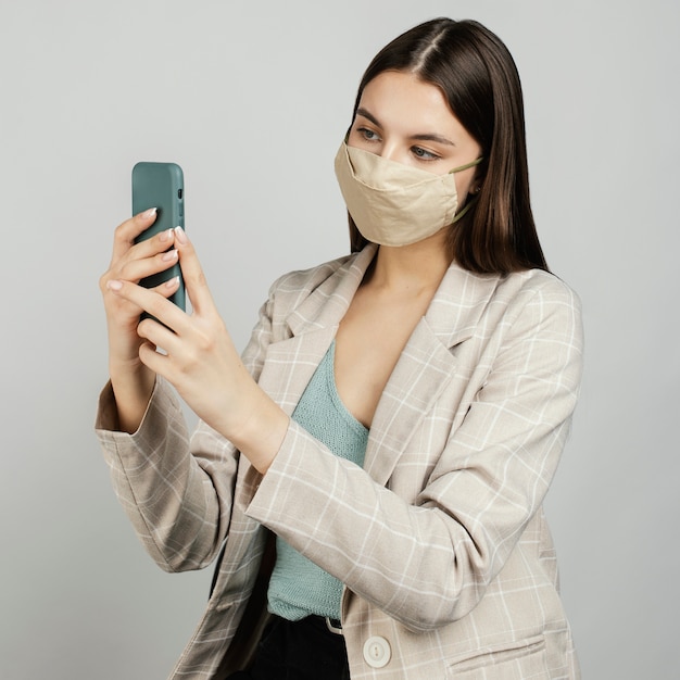 Portret stijlvolle vrouw met masker met behulp van mobiel