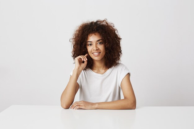 Portret van aantrekkelijk Afrikaans meisje dat over witte muur glimlacht