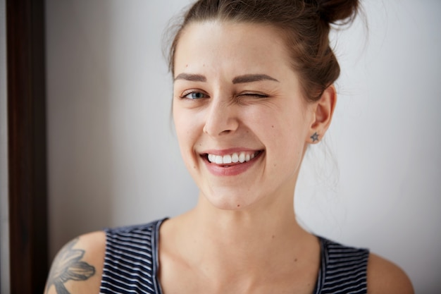 Portret van aantrekkelijke leuke vrouw die over grijze muur knipoogt