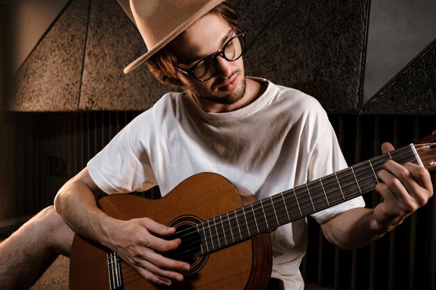 Portret van aantrekkelijke mannelijke muzikant die aandachtig op gitaar speelt in de opnamestudio. Knappe stijlvolle man componeert lied in moderne geluidsstudio