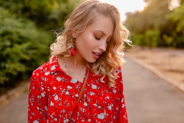 Portret van aantrekkelijke modieuze blonde glimlachende vrouw in rode de manieruitrusting die van de blousezomer oorringen het glimlachen dragen