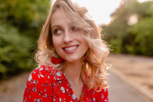 Portret van aantrekkelijke modieuze blonde glimlachende vrouw in rode de manieruitrusting die van de blousezomer oorringen het glimlachen dragen