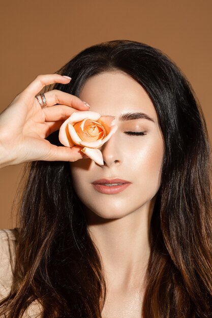 Portret van aantrekkelijke sensuele vrouw met donker haar met gesloten ogen met rosebud in de hand tegen een van haar ogen.