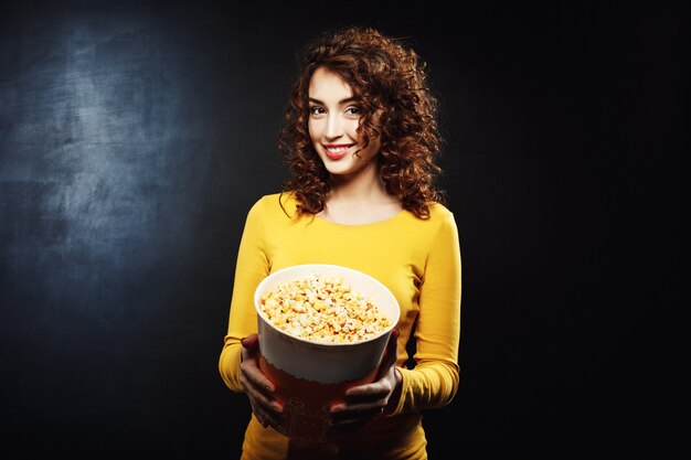 Portret van aantrekkelijke vrouw die aan popcorn met vrolijke glimlach behandelt