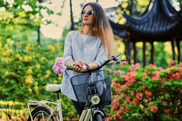 Portret van aantrekkelijke vrouw met stadsfiets in de buurt van traditioneel Chinees paviljoen in een park.