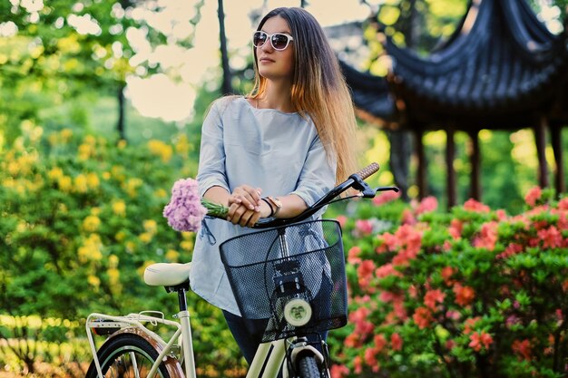 Portret van aantrekkelijke vrouw met stadsfiets in de buurt van traditioneel Chinees paviljoen in een park.