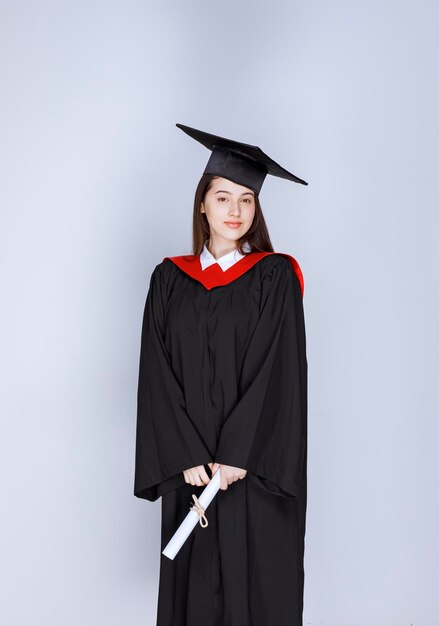 Portret van afgestudeerde student in toga met diploma en staande. Hoge kwaliteit foto