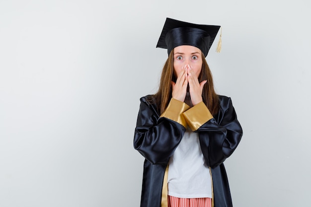 Gratis foto portret van afgestudeerde vrouw hand in hand op mond in vrijetijdskleding, uniform en op zoek geschokt vooraanzicht