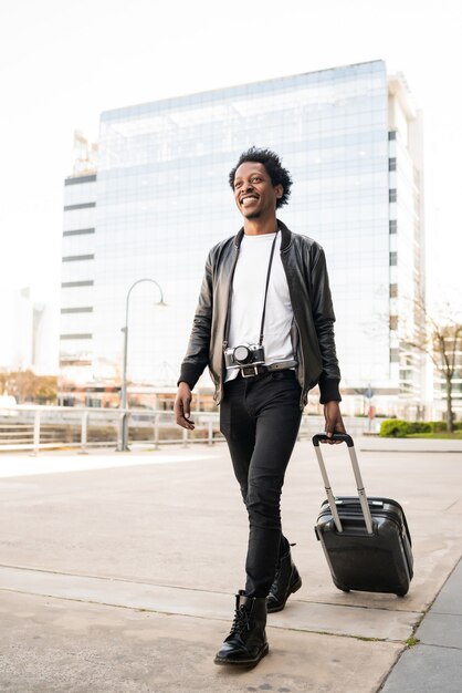 Portret van afro toeristische man met koffer tijdens het buiten lopen op straat. Toerisme concept.