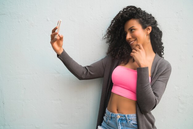 Portret van afrovrouw die selfies met haar mophile telefoon neemt tegen grijze muur. Technologie concept.