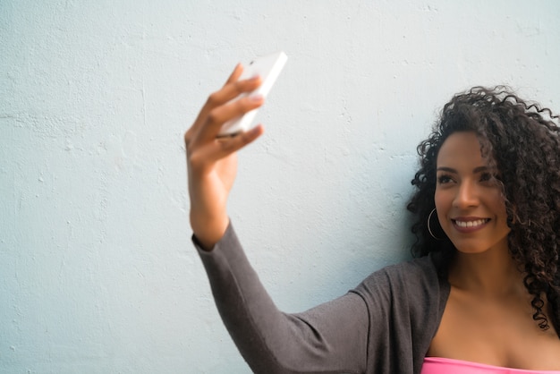 Portret van afrovrouw die selfies met haar mophile telefoon neemt tegen grijze muur. technologie concept.