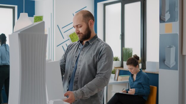 Portret van architect die een bouwmodel vasthoudt om architecturaal project en structuur te creëren. Man bouwer kijken naar maquette lay-out om bouwplan en stedelijke architectuur te ontwerpen.