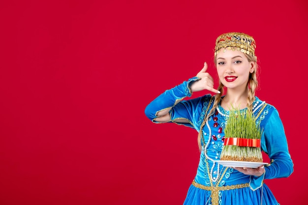 Gratis foto portret van azeri vrouw in traditionele kleding met groene semeni op rode achtergrond concept novruz lente etnische