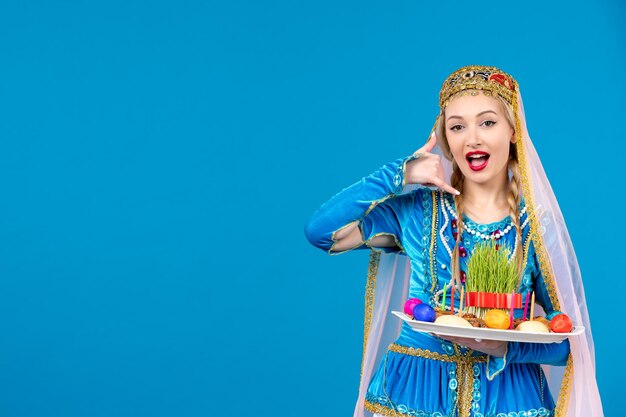 Portret van azeri vrouw in traditionele kleding met novruz xonca poseren op blauwe achtergrond voorjaar etnische geld