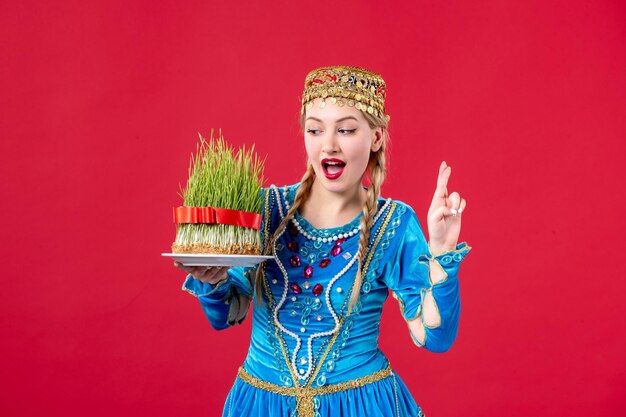 Gratis foto portret van azeri vrouw in traditionele kleding met semeni studio shot rode achtergrond etnische novruz vakantie concept