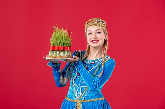 Gratis foto portret van azeri vrouw in traditionele kleding met semeni studio shot rode achtergrond novruz lentedanser