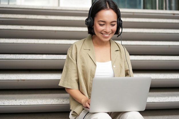 Portret van aziatische vrouw digitale nomade meisje met behulp van laptop en luistert naar muziek buitenshuis jonge student