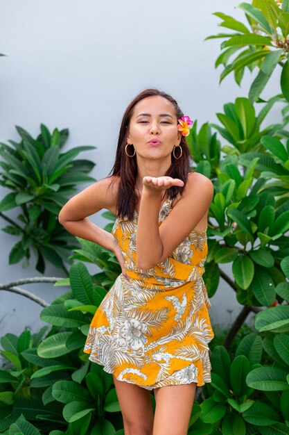 Portret van Aziatische vrouw in gele zomerjurk staat met plumeria Thaise bloem in haar en ronde oorbellen