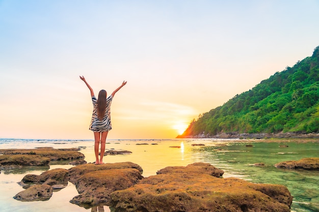 Portret van Aziatische vrouw op de rots met geopende wapens bij zonsondergang rond oceaan in vakantie