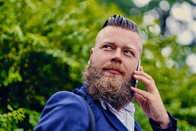 Portret van bebaarde hipster man met smartphone buiten.