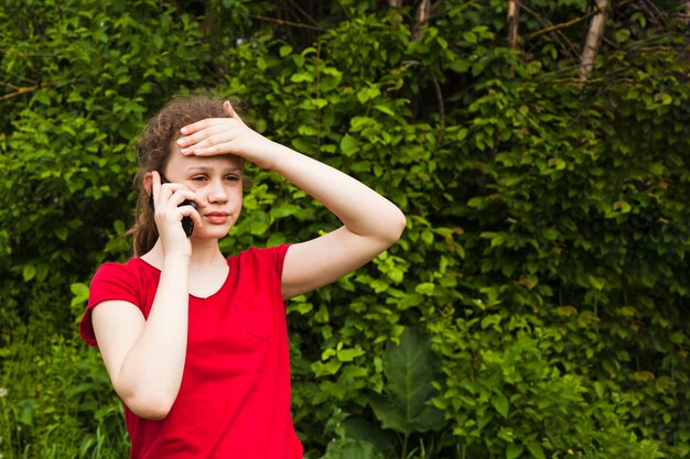 Portret van bezorgd mooi meisje dat op cellphone in park spreekt