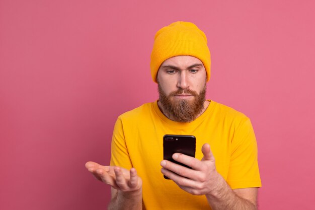 Portret van bezorgde geschokte volwassen bebaarde man hijgend ongelukkig met smartphone lezen vreemd en verontrustend bericht op roze