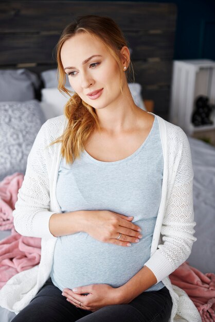 Portret van bezorgde zwangere vrouw die op bed zit