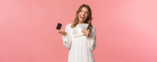 Portret van blij aantrekkelijk blond meisje in witte jurk dagdromen over wat kopen met gi