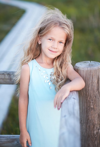 Gratis foto portret van blond schattig tienermeisje in een blauwe jurk over natuurlijke buitenveld.