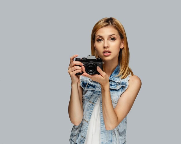 Portret van blonde vrouwelijke fotograaf geïsoleerd op een grijze achtergrond.