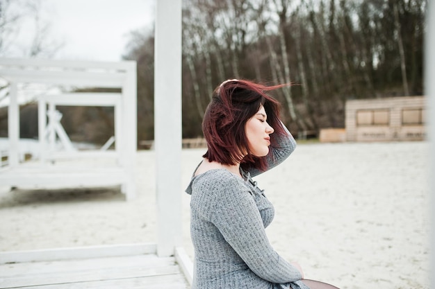 Portret van brunette meisje in grijze jurk zittend op witte houten constructie