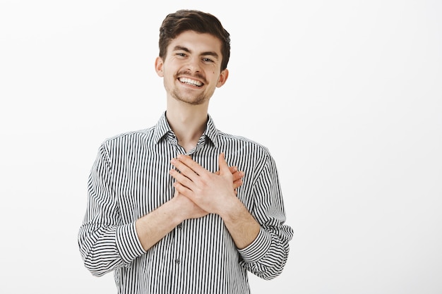 Portret van charmante gelukkig blanke man met baard en snor, handpalmen op het hart houden en glimlachen van tevredenheid, aangeraakt met mooi gebaar