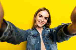 Gratis foto portret van cool vrolijk meisje schieten selfie op camera aan de voorkant geïsoleerd op gele muur