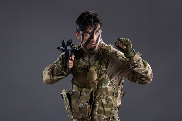 Portret van dappere soldaat in camouflage met machinegeweer op donkere muur