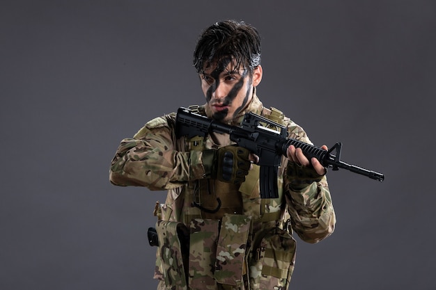 Portret van dappere soldaat in militair uniform met machinegeweer op donkere muur