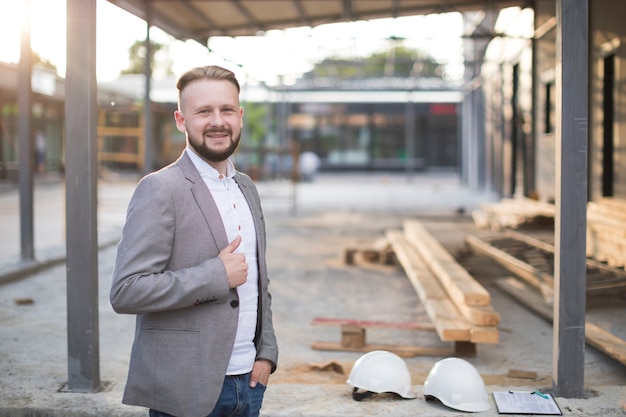 Gratis foto portret van de glimlachende jonge architectenman die duim op gebaar tonen die camera bekijken