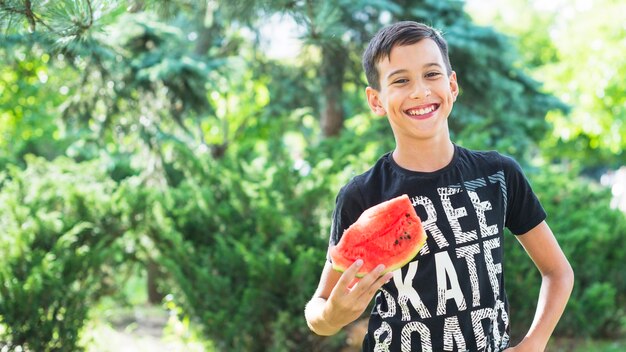 Portret van de glimlachende plak van de jongensholding van watermeloen in openlucht