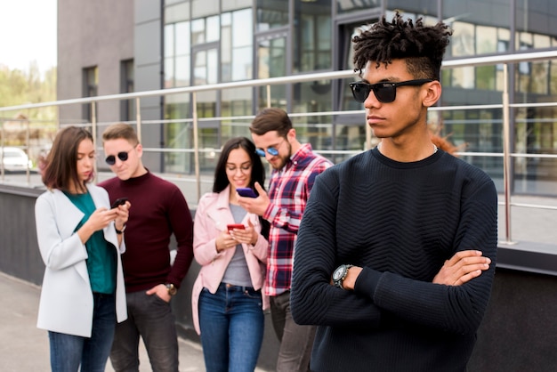 Portret van de jonge afrikaanse mens die terwijl zijn vrienden bezig in mobiele telefoon stelt