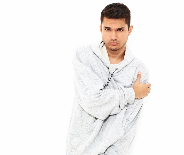 Portret van de jonge knappe modelmens gekleed in grijze toevallige hoodiekleren die op witte muur stellen. Geïsoleerd